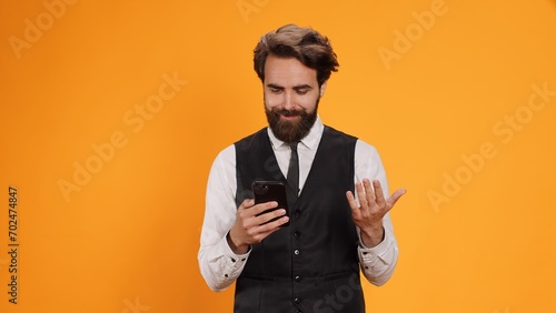 Professional waiter checking phone before serving customers at restaurant table. Luxurious stylish butler working in culinary sector, reading texts on social media app, formal service. photo