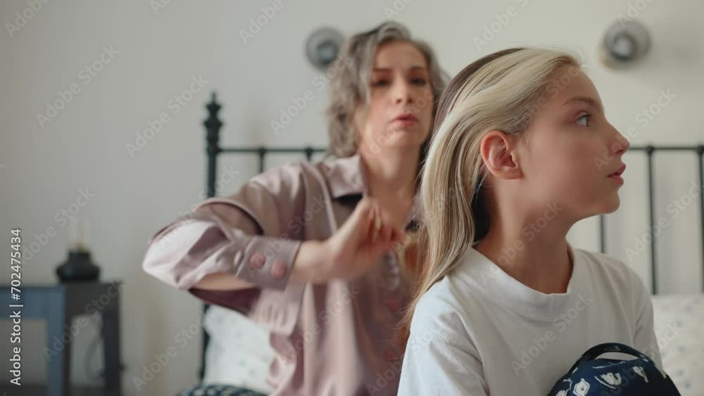 Concentrated gray haired young mom brushing her daughters hair at home in morning Concentrated gray haired young mom brushing her daughters hair at home in morning