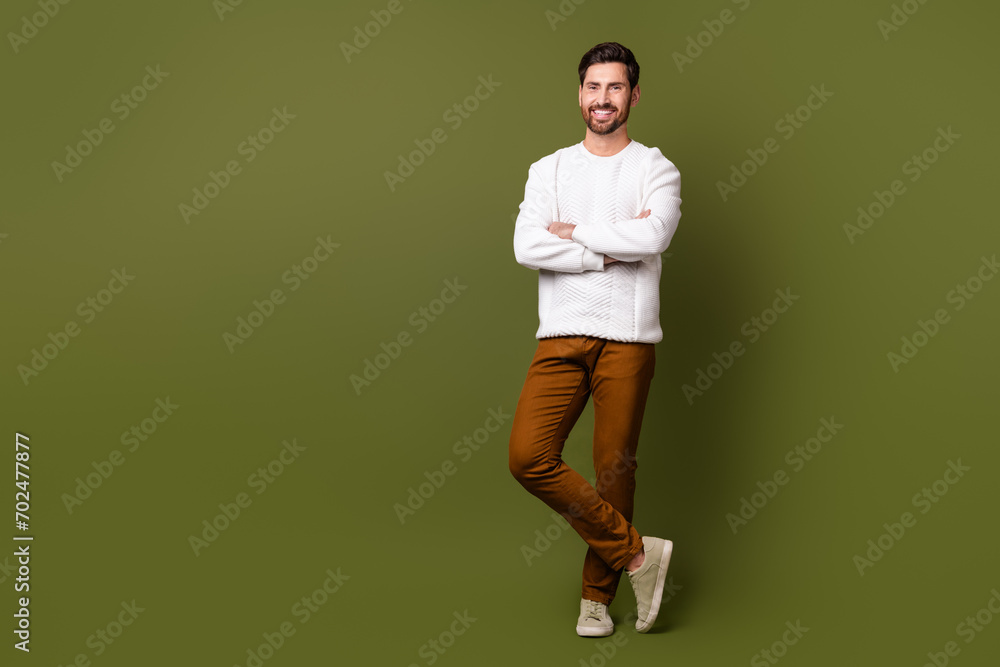 Full length photo of cheerful smiling man crossed arms standing billboard empty space isolated on khaki color background Full length photo of cheerful smiling man crossed arms standing billboard empty space isolated on khaki color background