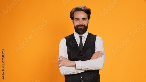 Before serving meal, elegant waiter poses with reliability in front of a yellow background in studio. Bearded server in suit operating in formal environment in the culinary sector.