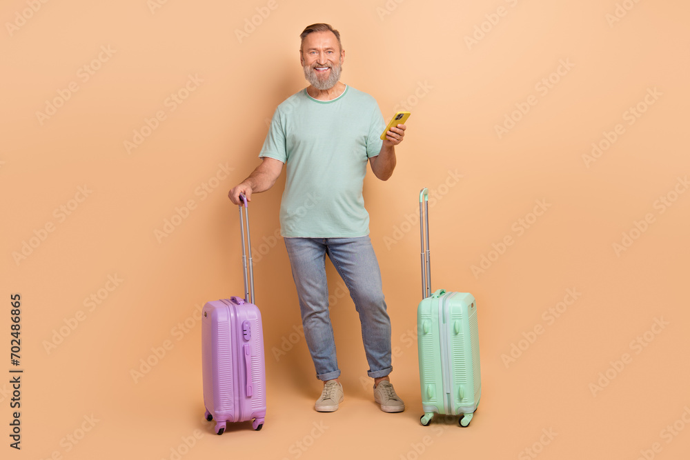 Full size portrait of handsome grandfather hold suitcase use smart phone isolated on beige color background Full size portrait of handsome grandfather hold suitcase use smart phone isolated on beige color background