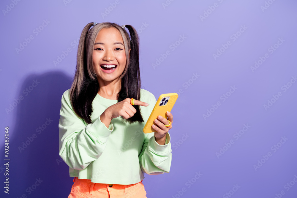 Photo of kpop fan youngster girl wearing green sweatshirt point finger demonstrating mobile phone isolated on purple color background Photo of kpop fan youngster girl wearing green sweatshirt point finger demonstrating mobile phone isolated on purple color background