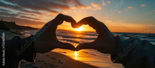 Lovers creating heart shape at sunrise with their fingers.