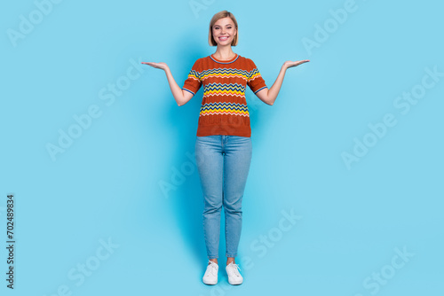 Full length photo of adorable lovely girl wear strited t-shirt palms presenting objects empty space isolated on blue color background photo