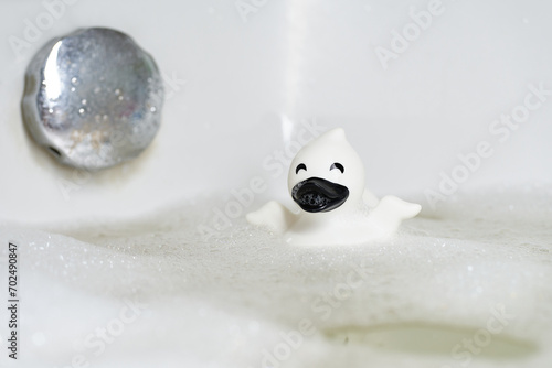 White and black rubber duck in a bathtub with foam close-up. Bright light, relaxing atmosphere