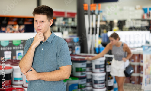 Thoughtful man standing in paint supplies store and planning to paint walls in apartment during renovation