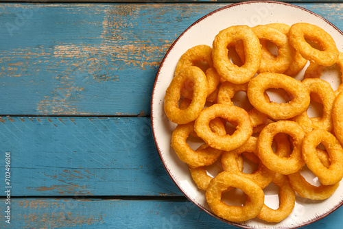 Plate with fried breaded onion rings on blue wooden background photo