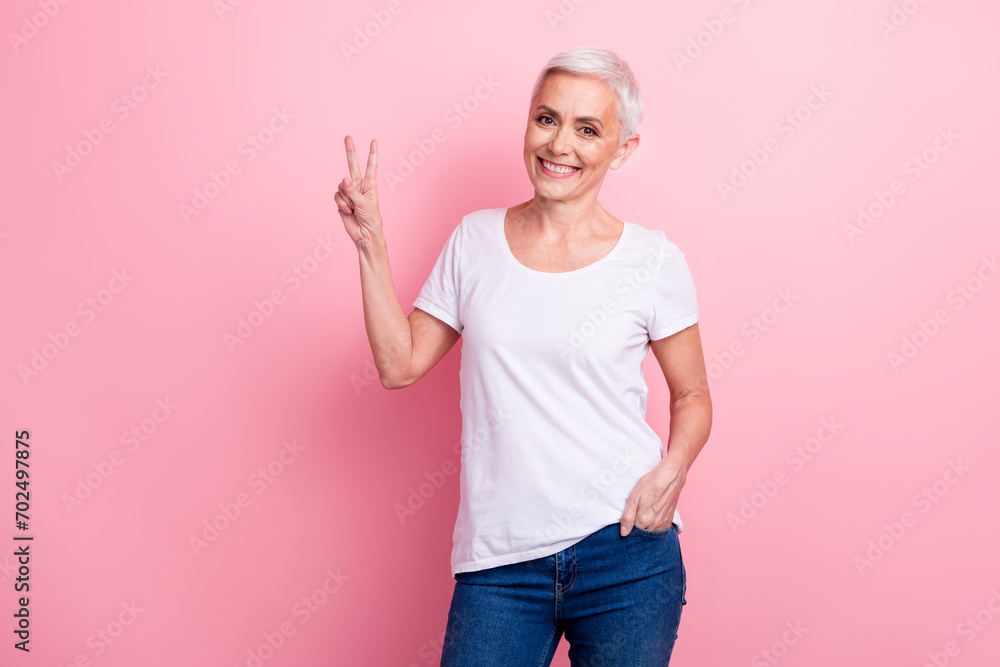 Portrait of cheerful friendly person with white hairdo dressed stylish t-shirt arm in pocket show v-sign isolated on pink background Portrait of cheerful friendly person with white hairdo dressed stylish t-shirt arm in pocket show v-sign isolated on pink background