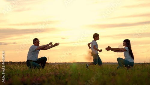Child Boy runs from father to mother on meadow in evening. Kid with parents spends time together on field at sunset twilight. Boy runs from father to mother reaching out arms in embrace. Happy family