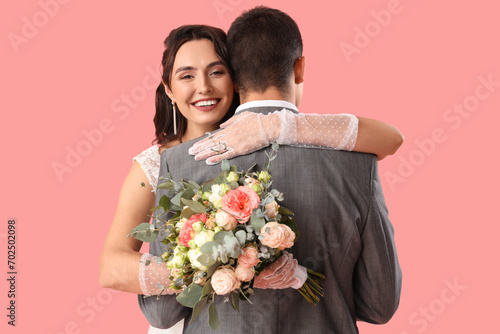 Young wedding couple with bouquet of flowers hugging on pink background