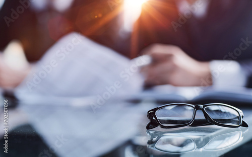 Close-up of eyeglasses on an office desk against a blurred background of employees