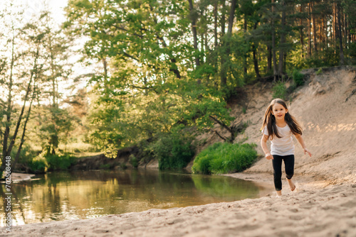 Happy little girl running on sandy beach close to river. Junior active athlete doing sports and having fun near water.