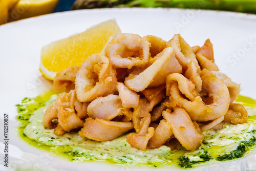 Deep fried squid rings or calamari with sauce and lemon on white plate.