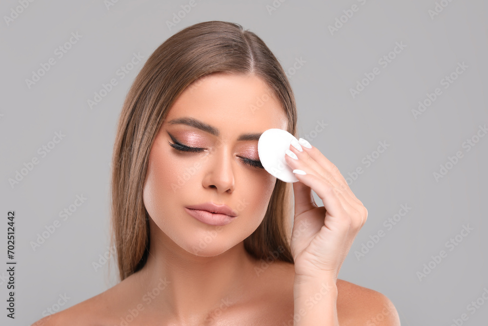 Beautiful woman removing makeup with cotton pad on grey background Beautiful woman removing makeup with cotton pad on grey background