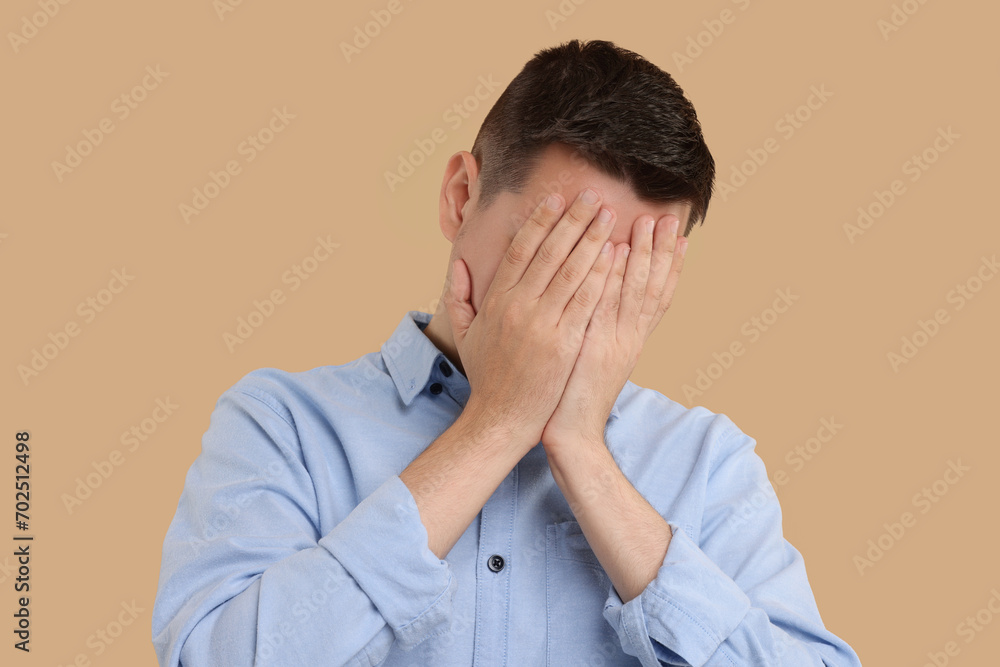 Resentful man covering face with hands on beige background Resentful man covering face with hands on beige background