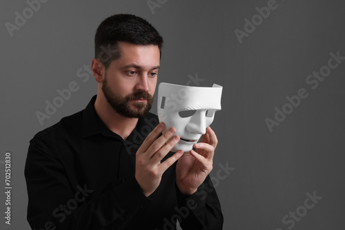 Multiple personality concept. Man putting on mask against grey background. Space for text © New Africa