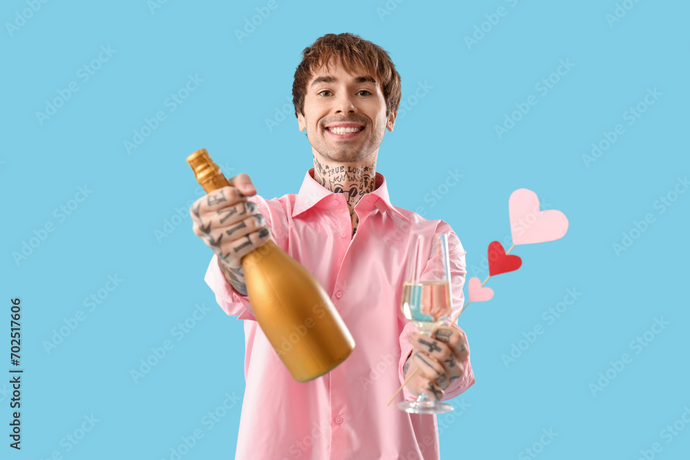 Handsome young man holding bottle and glass of champagne with paper hearts on blue background. Valentine's day celebration Handsome young man holding bottle and glass of champagne with paper hearts on blue background. Valentine's day celebration