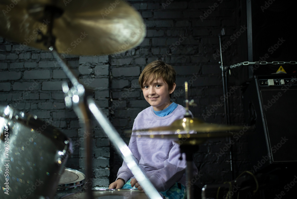 A 10 year old boy sits behind a silver drum kit. happy child learns to play the drums.