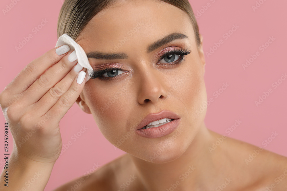 Beautiful woman removing makeup with cotton pad on pink background, closeup