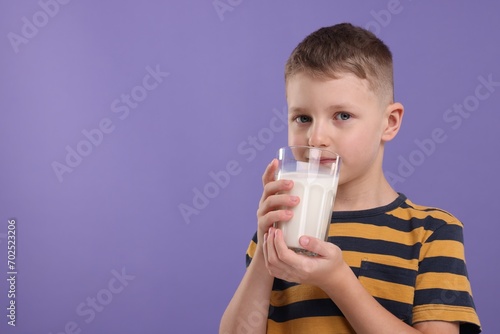 Cute boy drinking fresh milk from glass on violet background, space for text