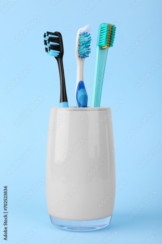 Different toothbrushes in holder on light blue background Different toothbrushes in holder on light blue background
