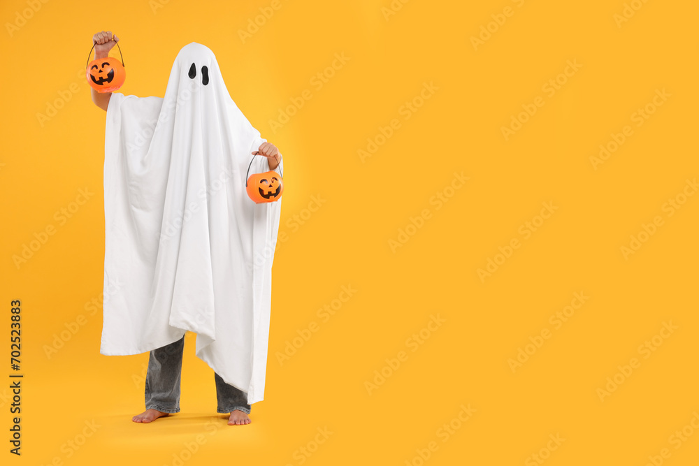 Woman in white ghost costume holding pumpkin buckets on yellow background, space for text. Halloween celebration - obrazy, fototapety, plakaty 