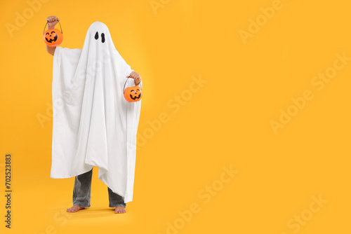 Fototapeta Woman in white ghost costume holding pumpkin buckets on yellow background, space for text