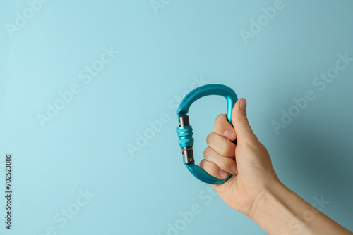 Woman with metal carabiner on light blue background, closeup. Space for text