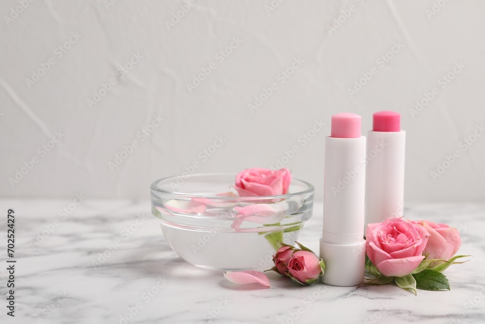 Lip balms, bowl with water and roses on white marble table, space for text Lip balms, bowl with water and roses on white marble table, space for text