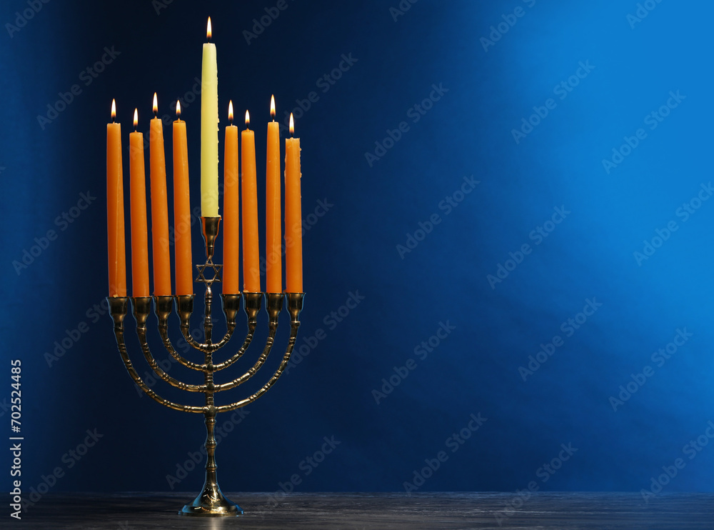 Hanukkah celebration. Menorah with burning candles on table against blue background, space for text Hanukkah celebration. Menorah with burning candles on table against blue background, space for text