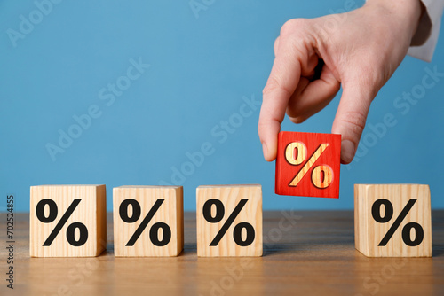 Best mortgage interest rate. Woman putting red cube with percent sign among others on wooden table, closeup