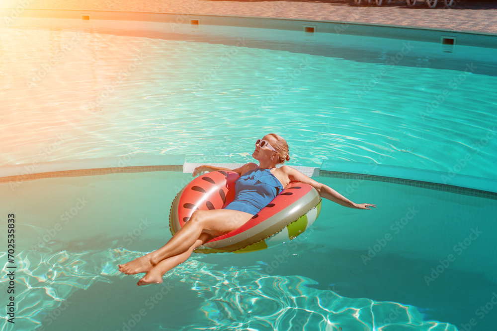 Happy woman in a swimsuit and sunglasses floating on an inflatable ring in the form of a watermelon, in the pool during summer holidays and vacations. Summer concept.