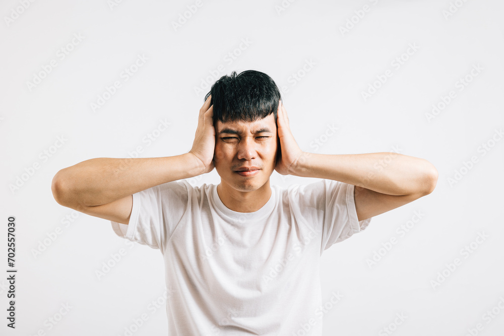 A man experiencing pain, desperately covering his ears with his hands and closing his eyes to escape the shouting noise. Studio shot isolated on white, illustrating his distress. A man experiencing pain, desperately covering his ears with his hands and closing his eyes to escape the shouting noise. Studio shot isolated on white, illustrating his distress.