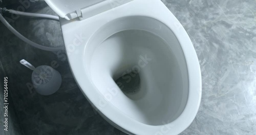 Toilet flush in bathroom. White ceramic clean toilet flushes water, toilet lid close slowly and carefully. Grey bathroom wc floor. Water flushes down. Flushing water in ceramic modern lavatory photo
