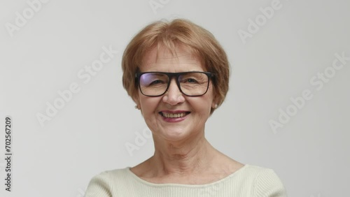 An elderly friendly woman in positive emotions with a charming smile wears eyeglasses to correct poor vision. A businesswoman chief or teacher in humorous mood, laughs and shows the gaze of a strict photo
