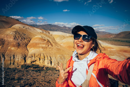Excited woman tourist takes a selfie with beautiful mountains view. Happy brunette having fun showing her tongue. Female portrait from vacation.