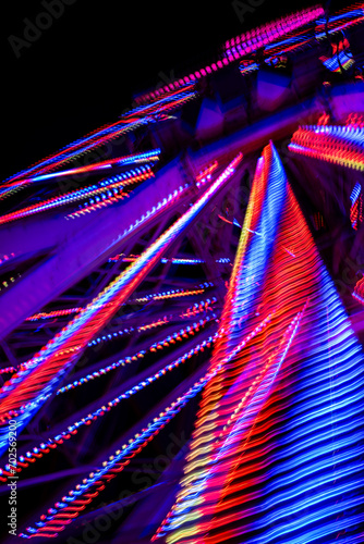 rainbow lights reflecting off the steel beams of a ferris wheel at night