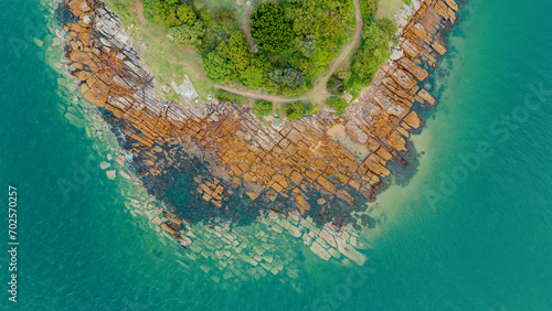overhead view from a drone of a cape or island on Sydney beach. The rocks are shown under the water of the turquoise green sea and the green vegetation of the island on a sunny day.
