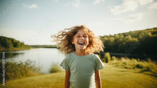 A happy little girl is laughing with joy on the background of a lake in summer. Concept of happiness, parenting, summertime and childhood