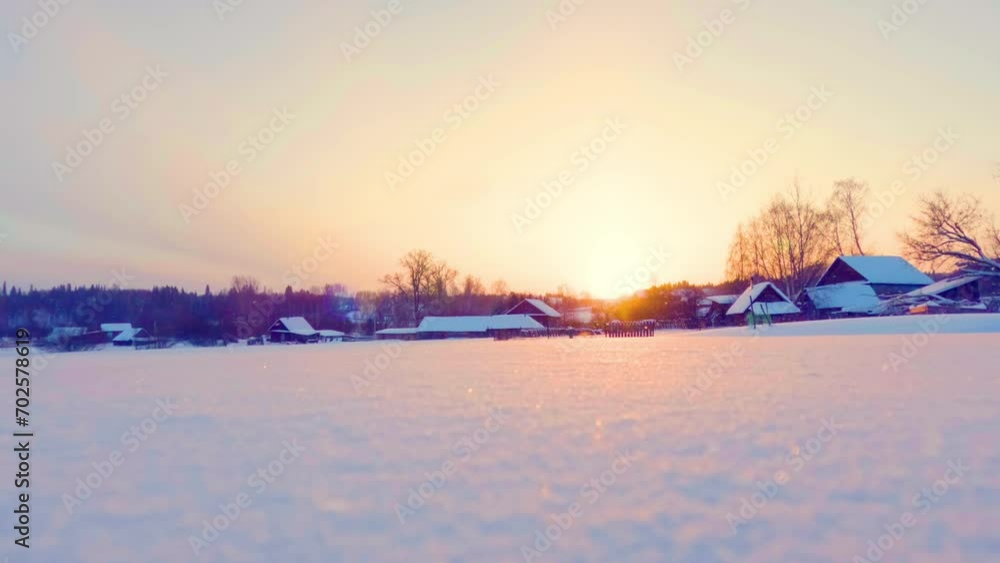 Winter Sunset over the roofs of farmhouses in the countryside. A huge snow field in the foreground. End of the day. Snowfall. Cinematic timelapse.