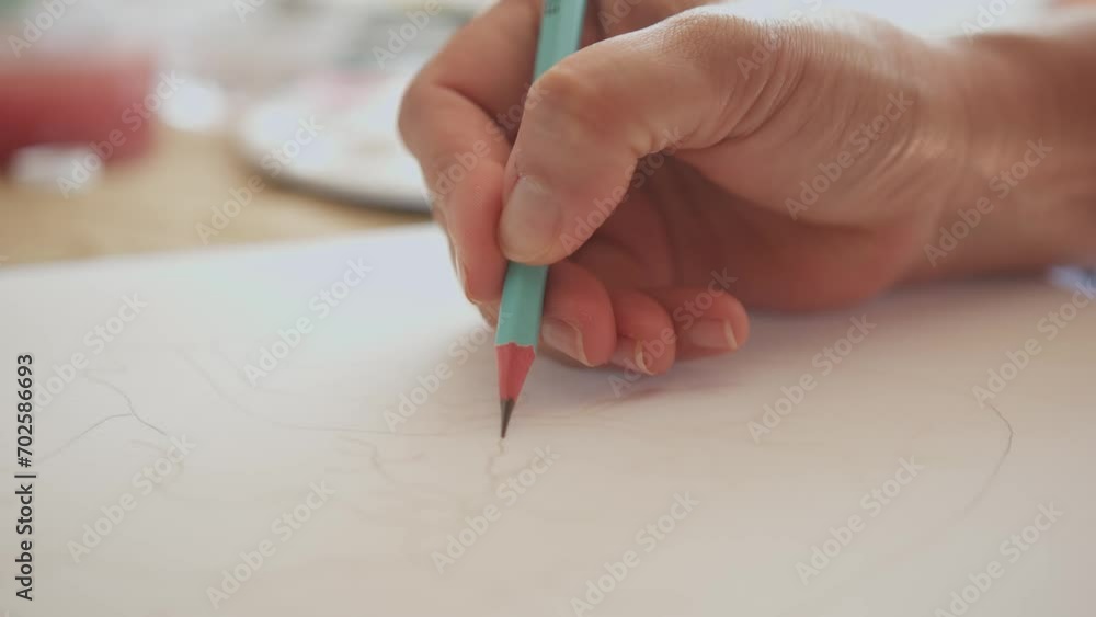 Hand holds teal pencil tracing and outlining flower pattern on watercolor paper Hand holds teal pencil tracing and outlining flower pattern on watercolor paper