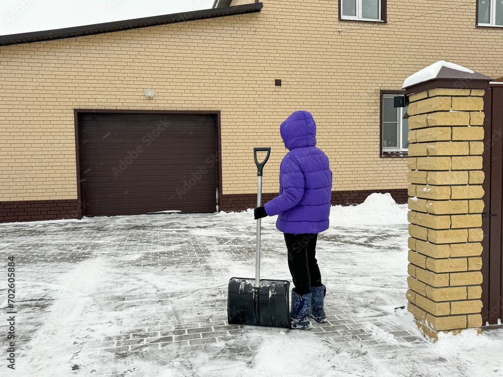 A girl cleans snow with a shovel in the courtyard of the house A girl cleans snow with a shovel in the courtyard of the house