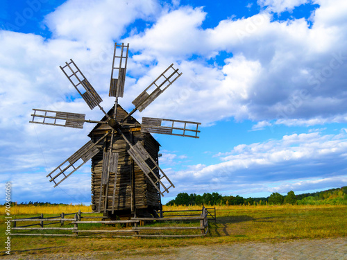 Photo of a windmill, taken in a picturesque rural landscape. A stationary windmill in windless weather. Horizontal image.