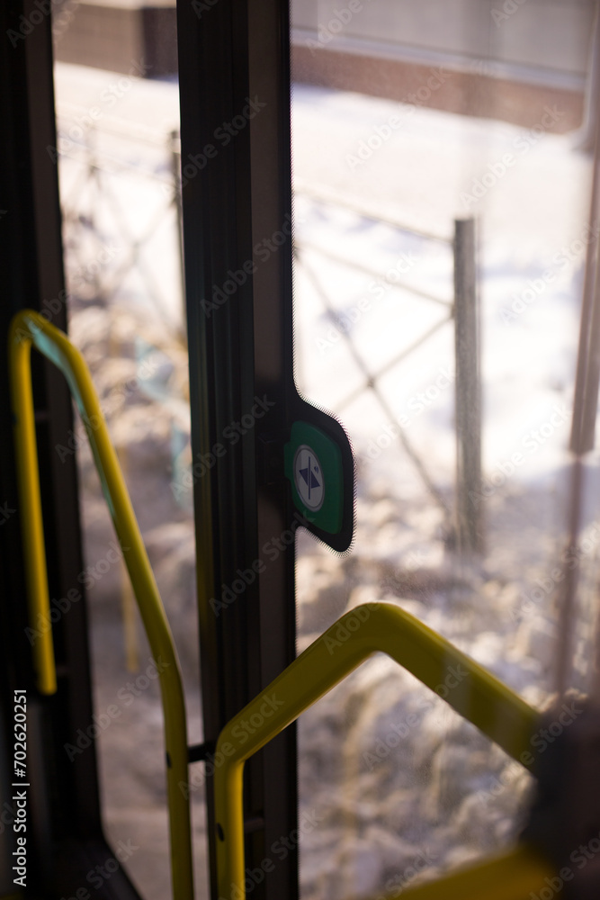 Door opening button on a modern bus. View from the interior of a public vehicle to the handrails on the glass doors