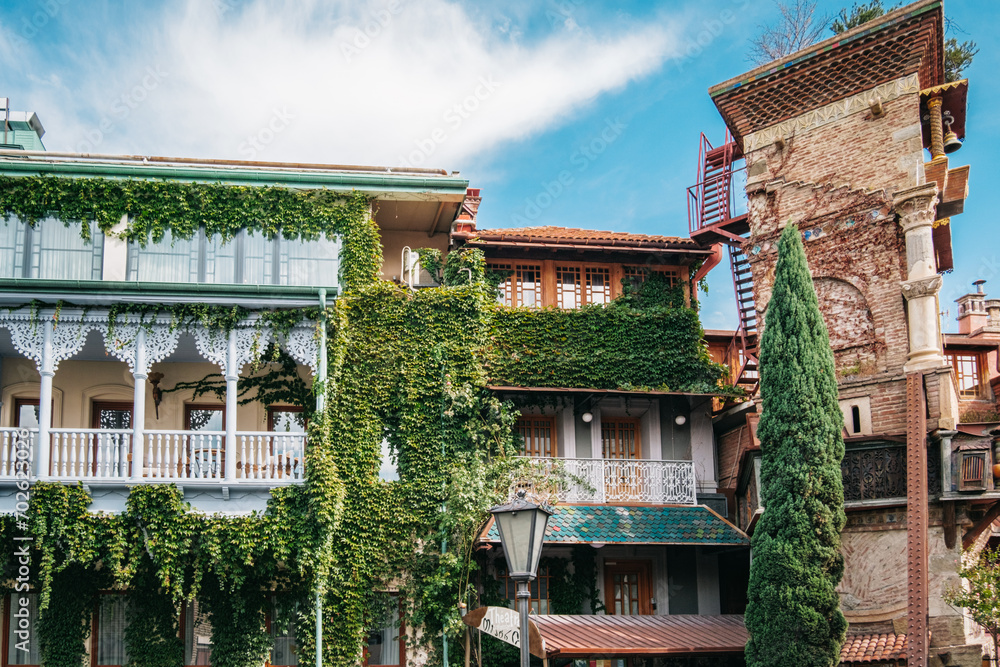 Beautiful traditional georgian house with vines climbing the wooden balcony next to the Leaning Clock Tower in Tbilisi Old town, Georgia