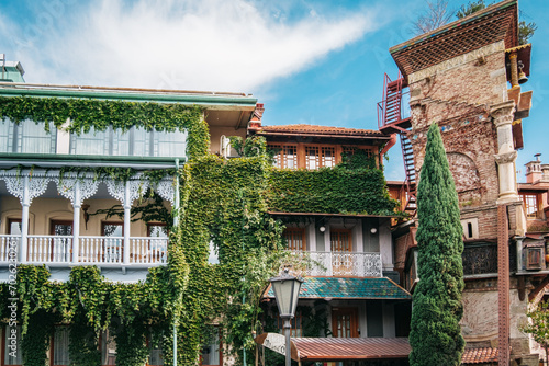 Beautiful traditional georgian house with vines climbing the wooden balcony next to the Leaning Clock Tower in Tbilisi Old town, Georgia