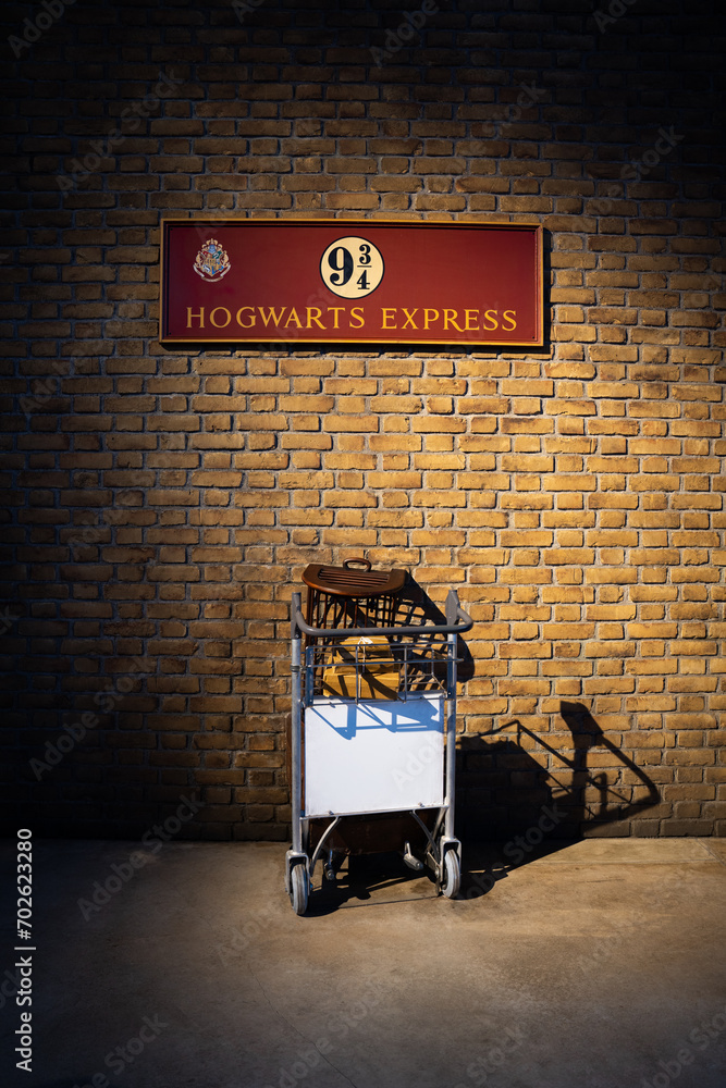 Naklejka premium JAPAN - NOV 13, 2023: Hogwarts Express platform 9¾ with owl bird cage and boxes in the shopping cart go to the wall, at Warner Bros. Studio Tour Tokyo, The Making of Harry Potter, Wizarding World
