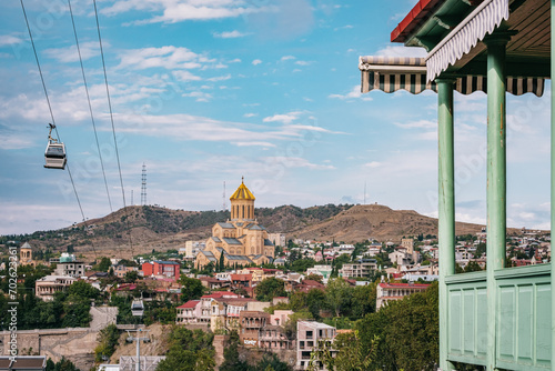 View of the Sameba Cathedral, the Tbilisi ropeway, and a traditional Georgian wooden balcony in Tbilisi
