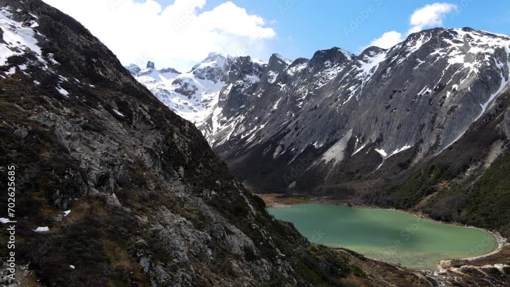 Drone shot flying along the mountainside to reveal the Laguna Esmeralda near Ushuaia, Argentina and the snow-covered Andes. Drone shot flying along the mountainside to reveal the Laguna Esmeralda near Ushuaia, Argentina and the snow-covered Andes.