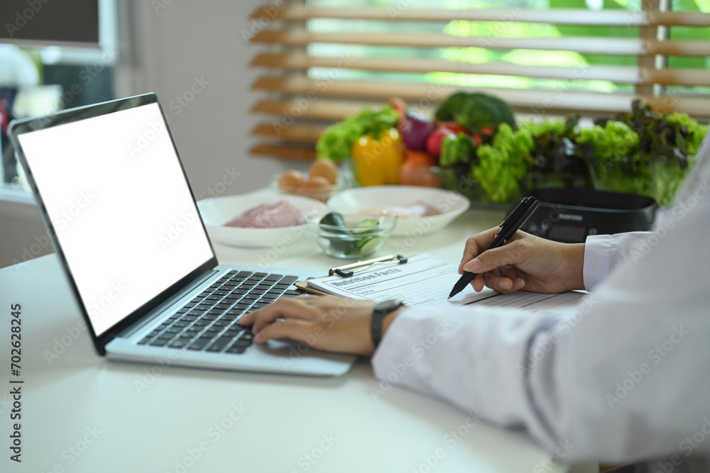 Closeup view professional nutritionist using laptop and prescribing recipe at working desk. - obrazy, fototapety, plakaty 